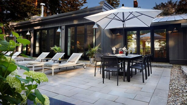 A modern outdoor patio with a dining table and chairs, surrounded by lounge chairs and potted plants.