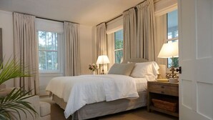 A bedroom with a bed, two bedside tables, a chair, and a window with curtains.