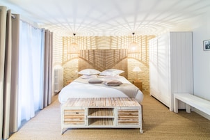 Un dormitorio con una cama grande, un banco de madera, un radiador fijado a la pared y un banco junto a la ventana.