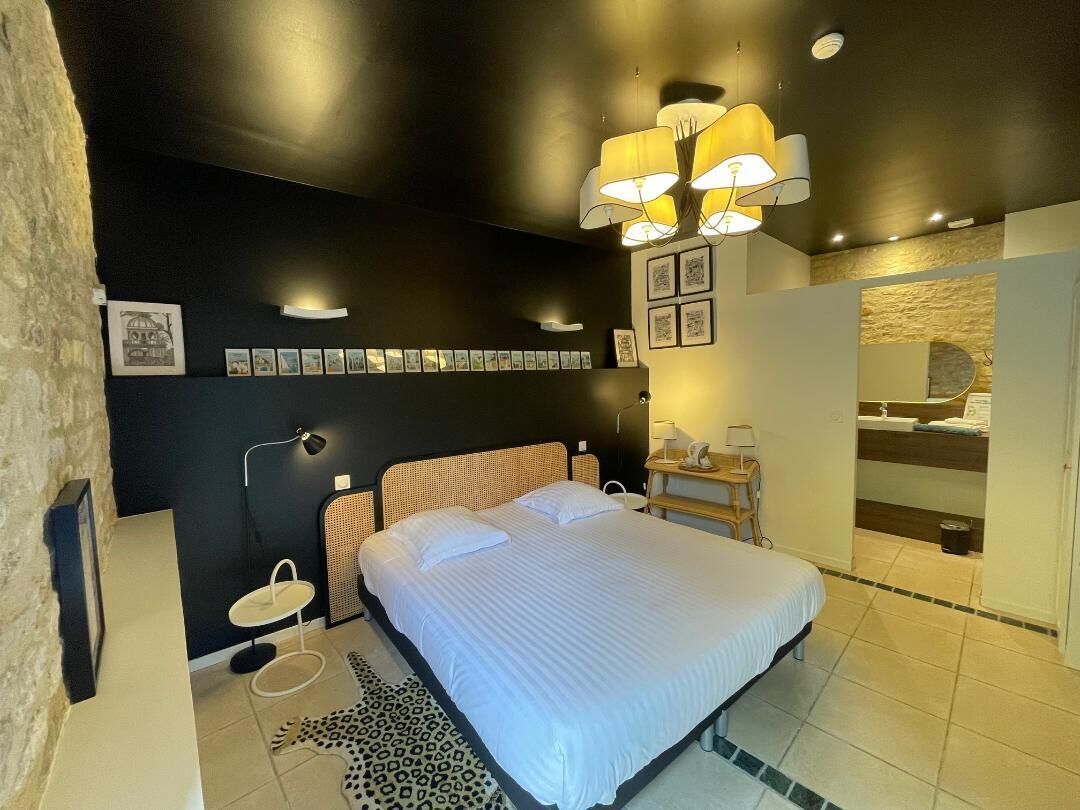 A modern bedroom with a large bed, a bedside table, a lamp, and a wall-mounted shelf with pictures.