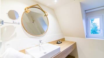 A modern bathroom with a large oval mirror, a white sink, and a wooden vanity.