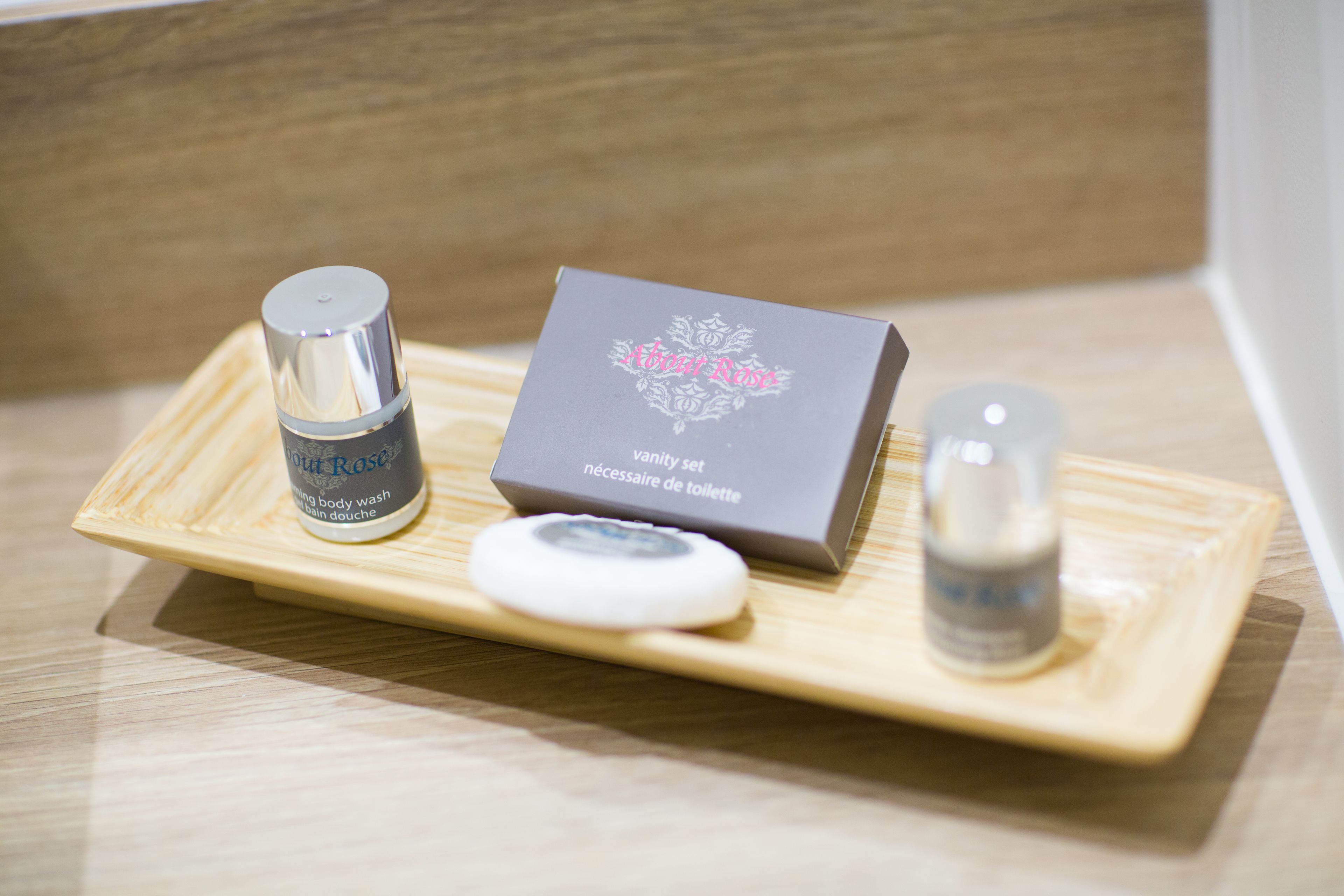 Ein Schminktisch-Set mit Duschgel, einer Seifenstange und einer kleinen Flasche, vermutlich mit Lotion oder Parfüm, auf einer Holzschale.