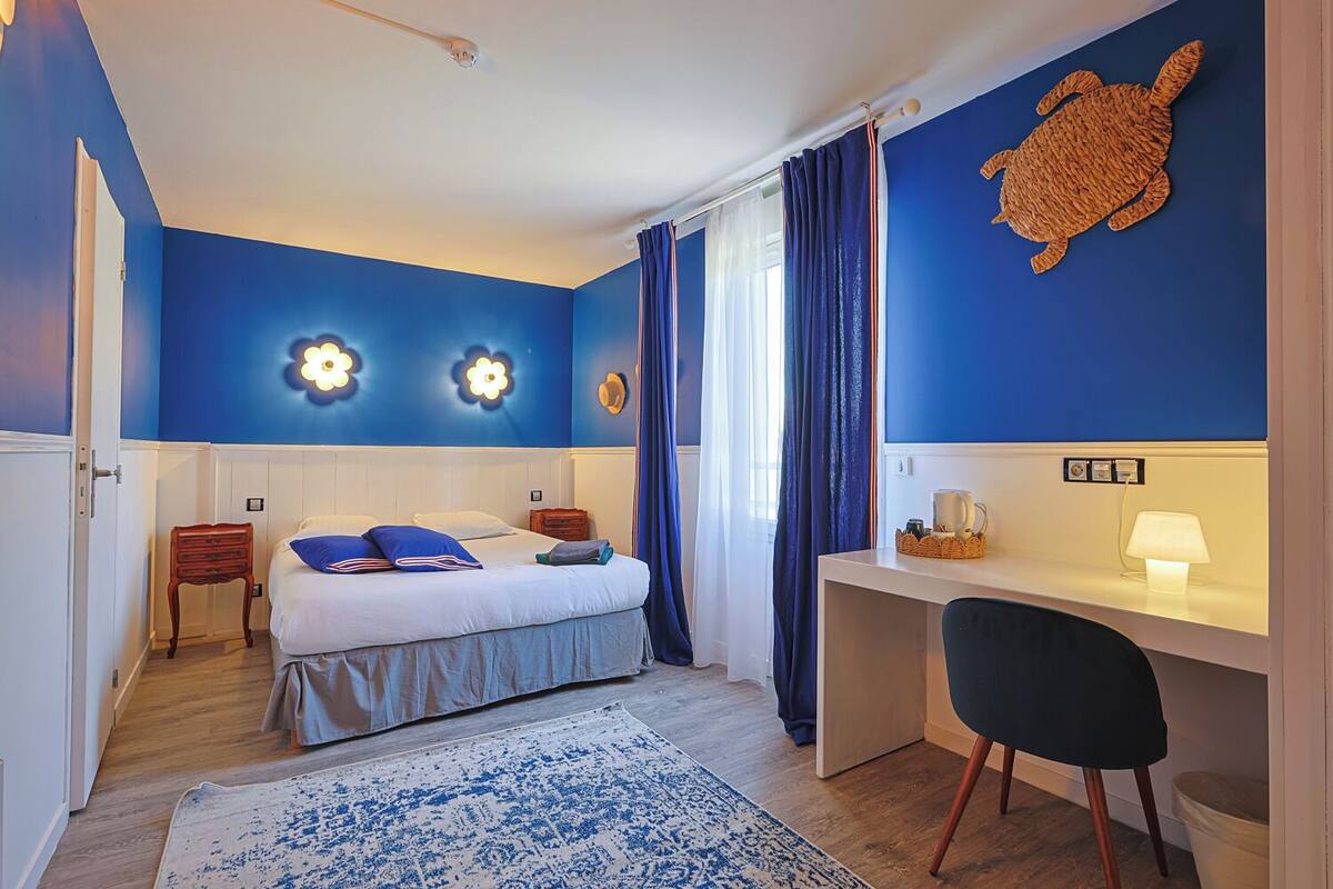 Een slaapkamer met een bed, een bureau, een stoel, een bureaulamp en een schildering van een schildpad.