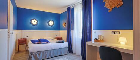 A bedroom with a bed, a desk, a chair, a desk lamp, and a turtle wall decoration.
