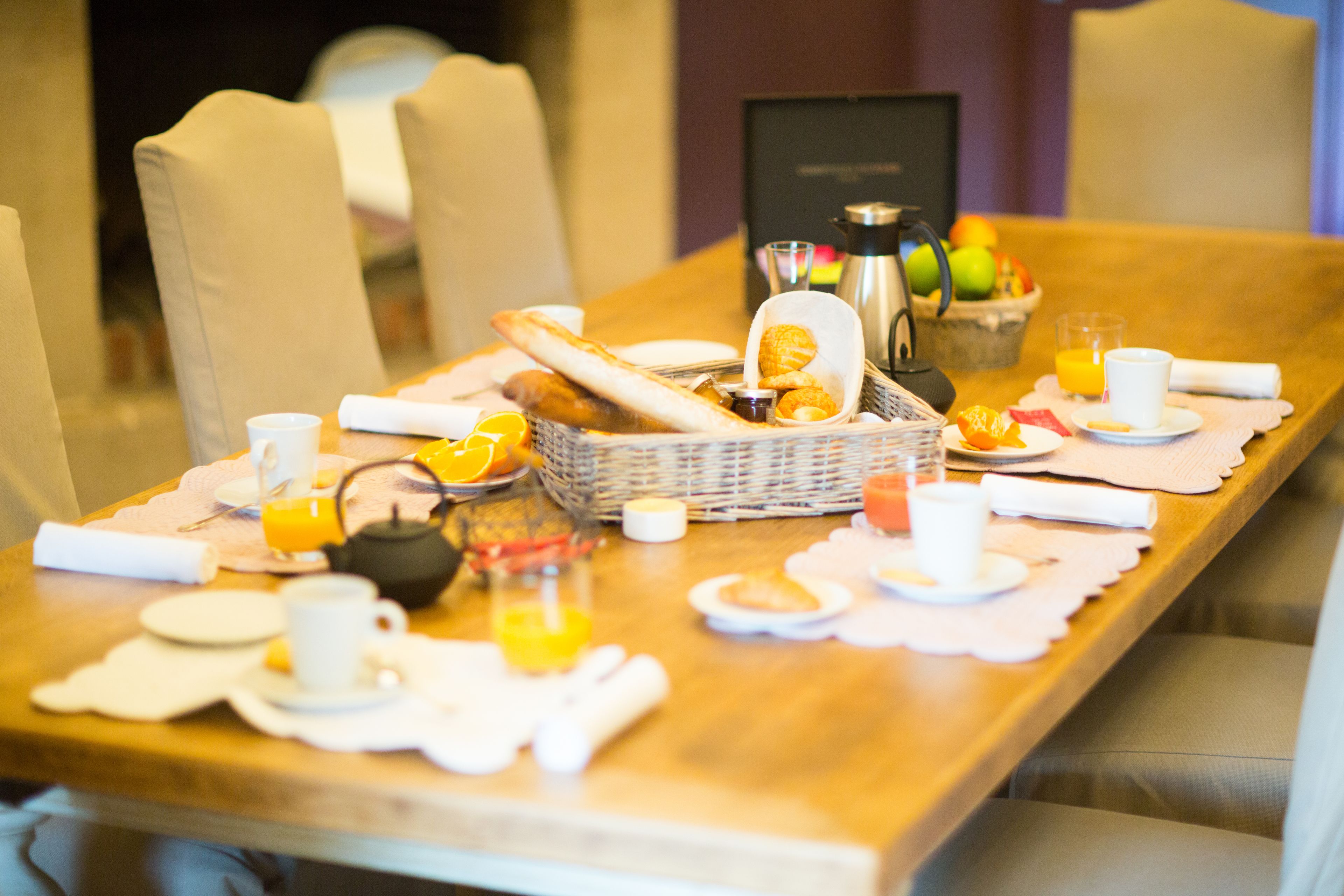 A breakfast setting with a table set for two, including bread, fruit, coffee, and tea.