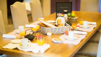 Een ontbijtsetting met een gedekte tafel voor twee personen, inclusief brood, fruit, koffie en thee.