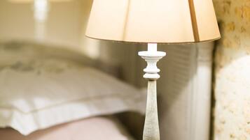 A bedside table with a lamp and a bed with pillows in the background.