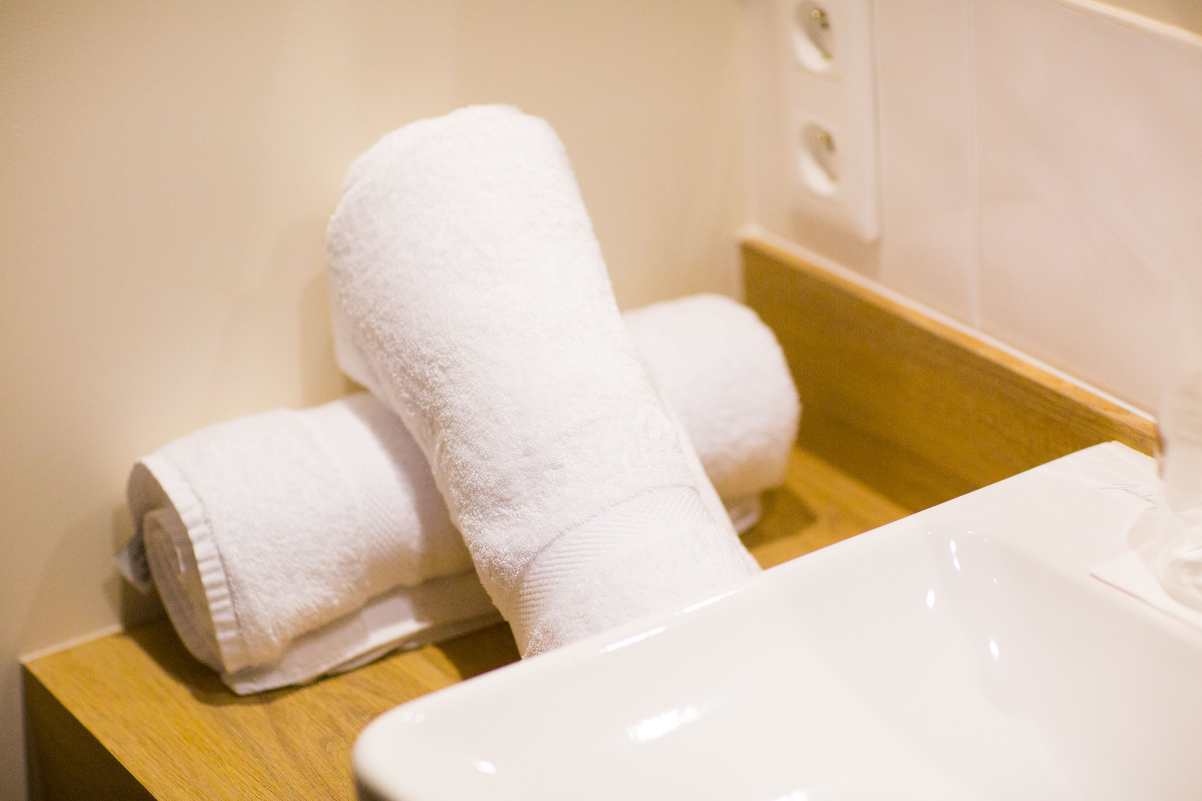 A bathroom with a white sink and two rolled towels on a wooden tray.