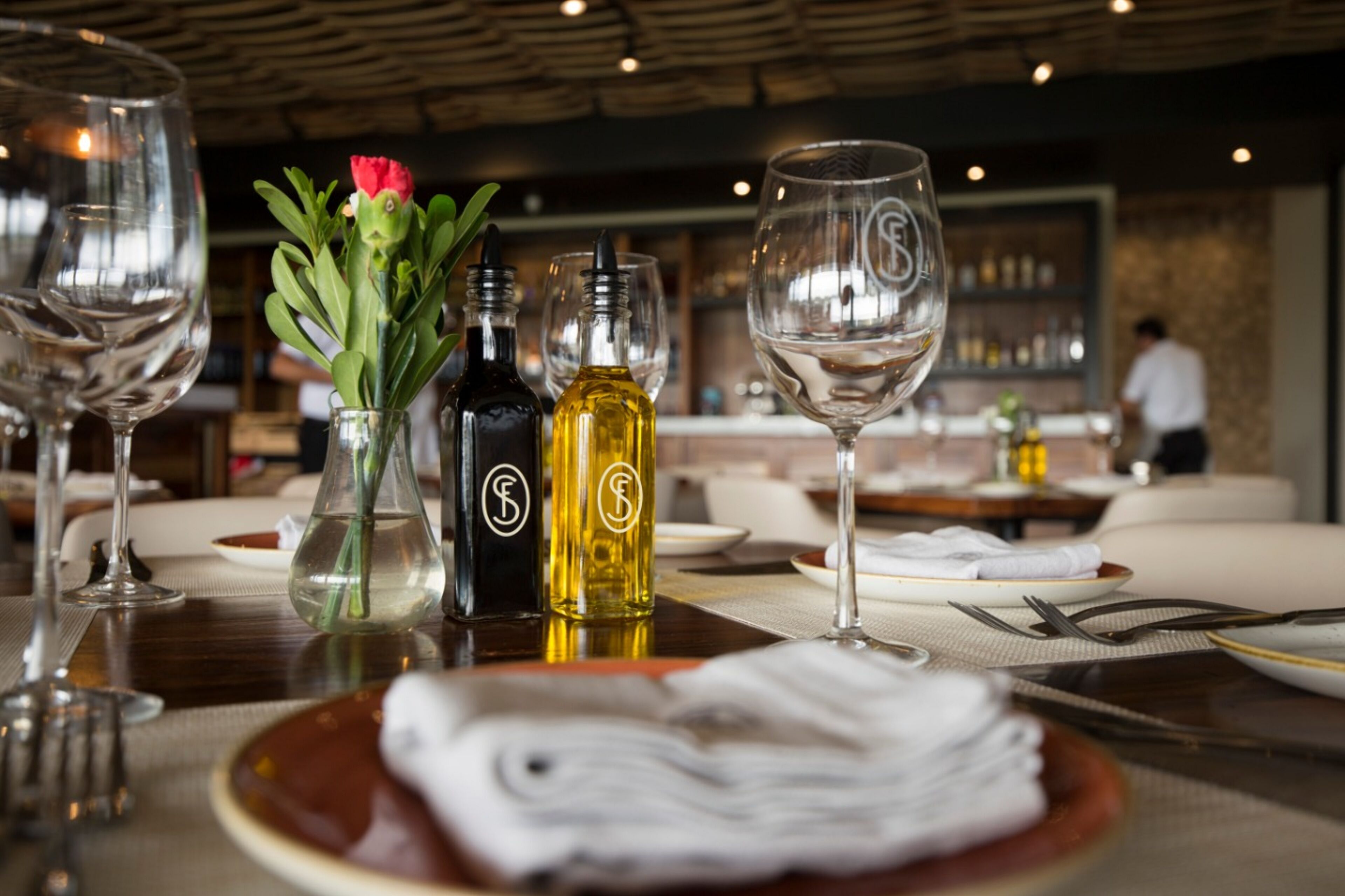 Une table à manger dressée avec des verres à vin, un vase contenant une fleur et des bouteilles de vin.