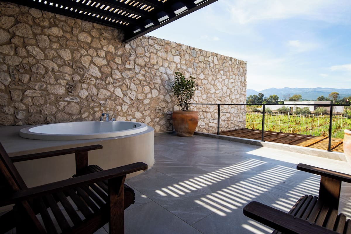 Un espacio al aire libre con paredes de piedra, una bañera grande, un banco de madera y una planta en maceta.