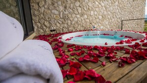 Een stenen muur, een hottub omringd met rozenblaadjes en een houten terras.