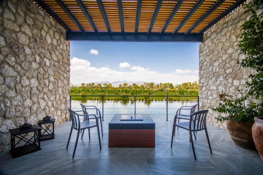 Un espace extérieur aménagé avec des murs en pierre, une pergola en bois et une vue sur un lac et des montagnes.