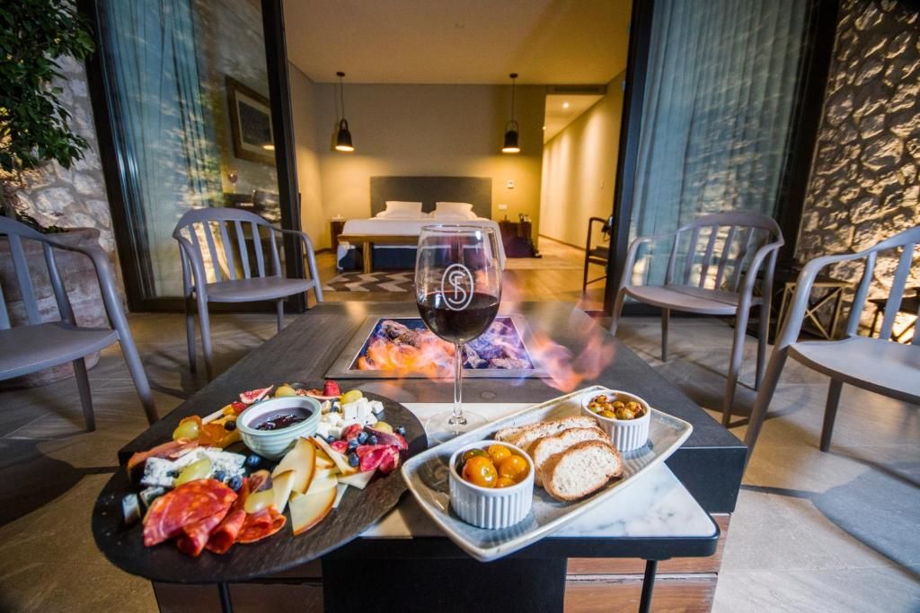 A dining area with a table set for two, featuring a variety of cheeses, fruits, and bread, with a glass of red wine.