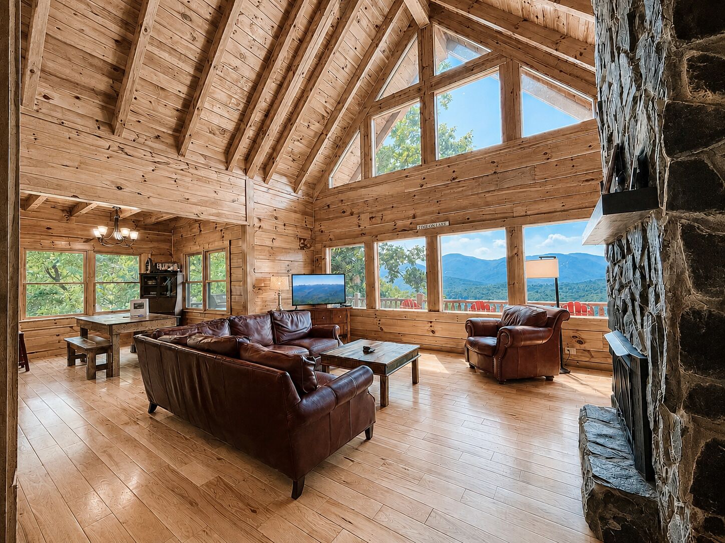 Une cabane en bois spacieuse, dotée d’un plafond haut, de grandes fenêtres et d’une cheminée en pierre.