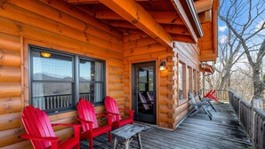 Uma cabana de madeira com um deque, cadeiras Adirondack vermelhas e um alpendre coberto.