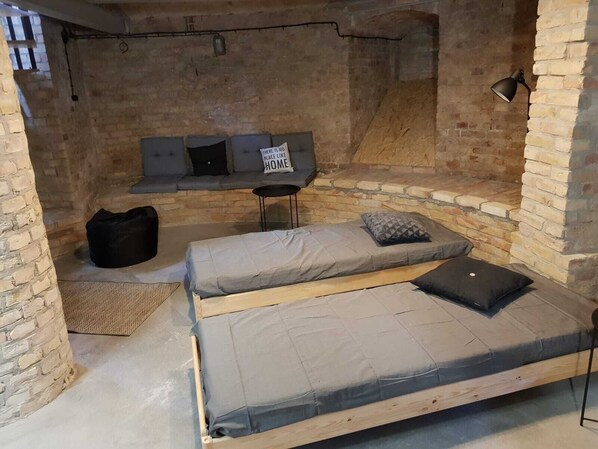 A cozy, rustic room with exposed brick walls, a loft bed, a small desk, and a bench with cushions.