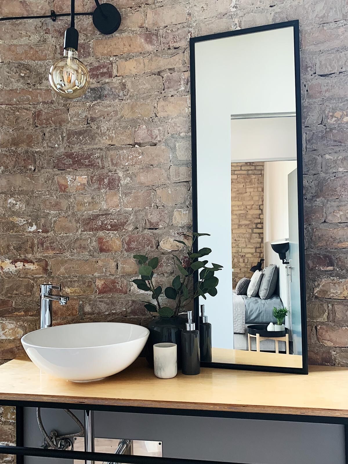 Une salle de bain avec un grand miroir, un lavabo blanc, un robinet noir et un luminaire suspendu.