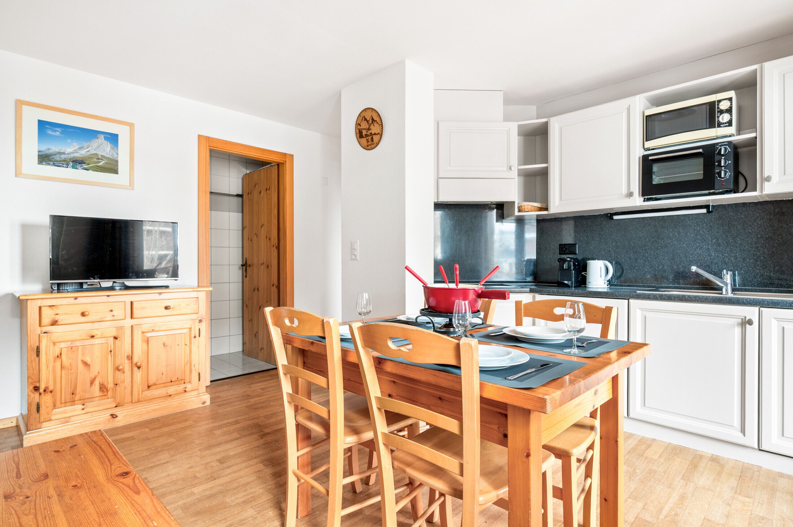A modern kitchen with white cabinets, a microwave, and a dining area with wooden chairs and a table set for two.