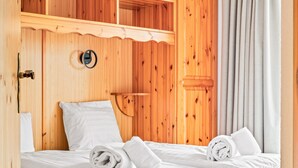 A wooden room with a bed, white linens, and a circular window.