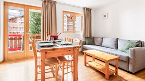 A living room with a wooden dining table, chairs, a grey sofa, and a wooden bench.
