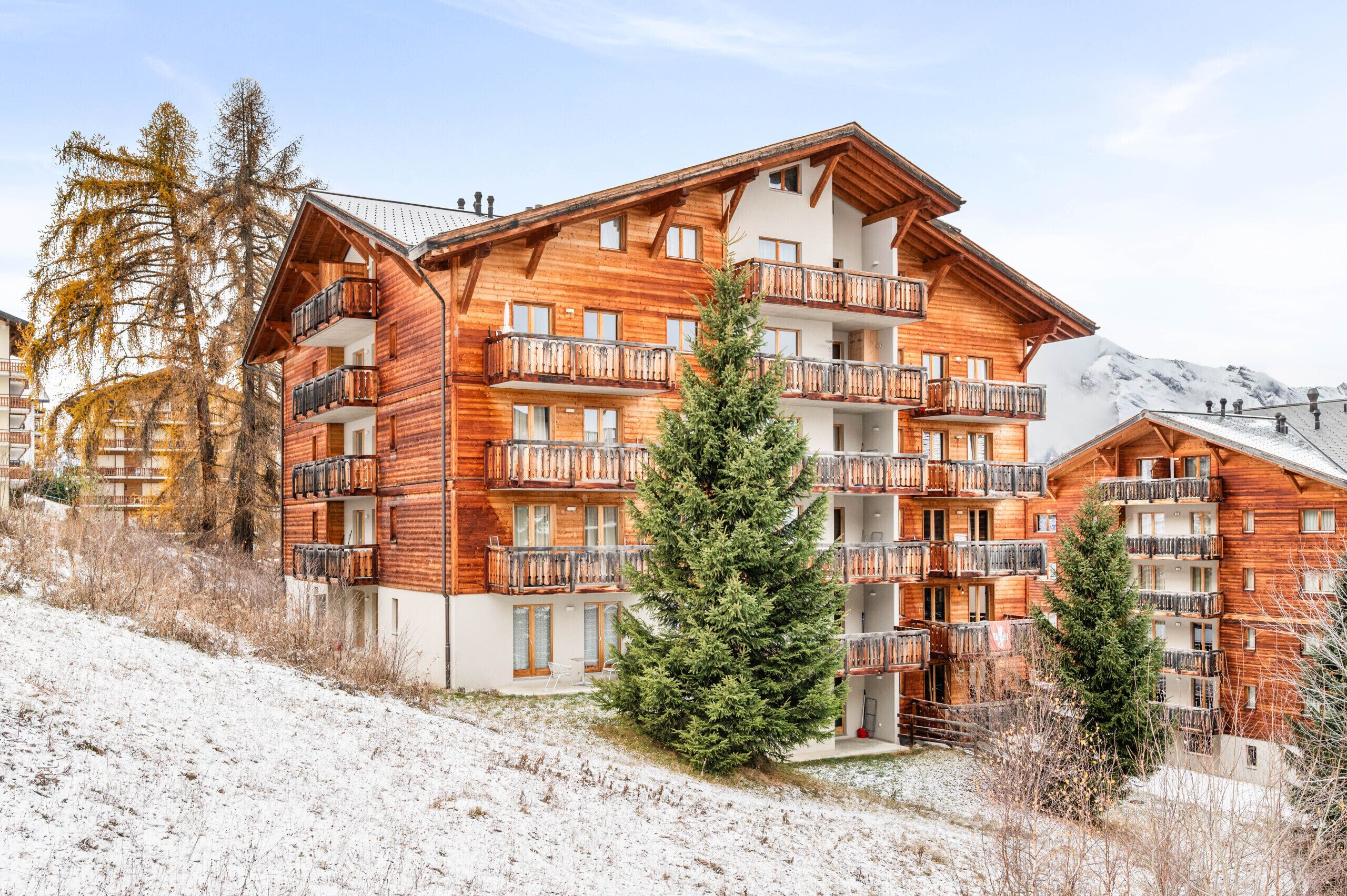 Un immeuble en bois à plusieurs étages, doté de balcons, entouré de neige et d’arbres.