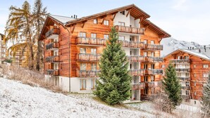 A multi-story wooden building with balconies, surrounded by snow and trees.