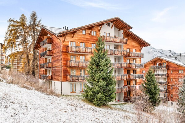 A multi-story wooden building with balconies, surrounded by snow and trees.