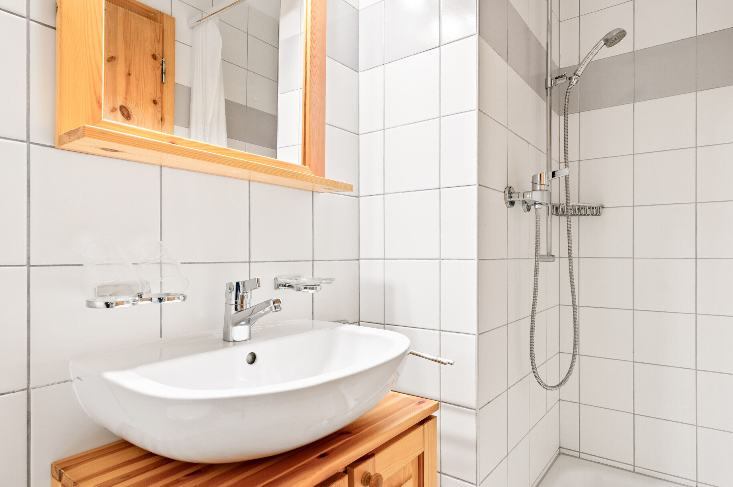 A bathroom with a white sink, a wooden vanity, a mirror, and a shower.