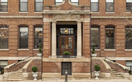 A brick building with a central entrance, large windows, and a staircase leading to the entrance.