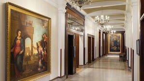 A long hallway with a large classical painting on the left, a chandelier, and a large framed painting at the end. - Celeste of St Paul (St. Paul)