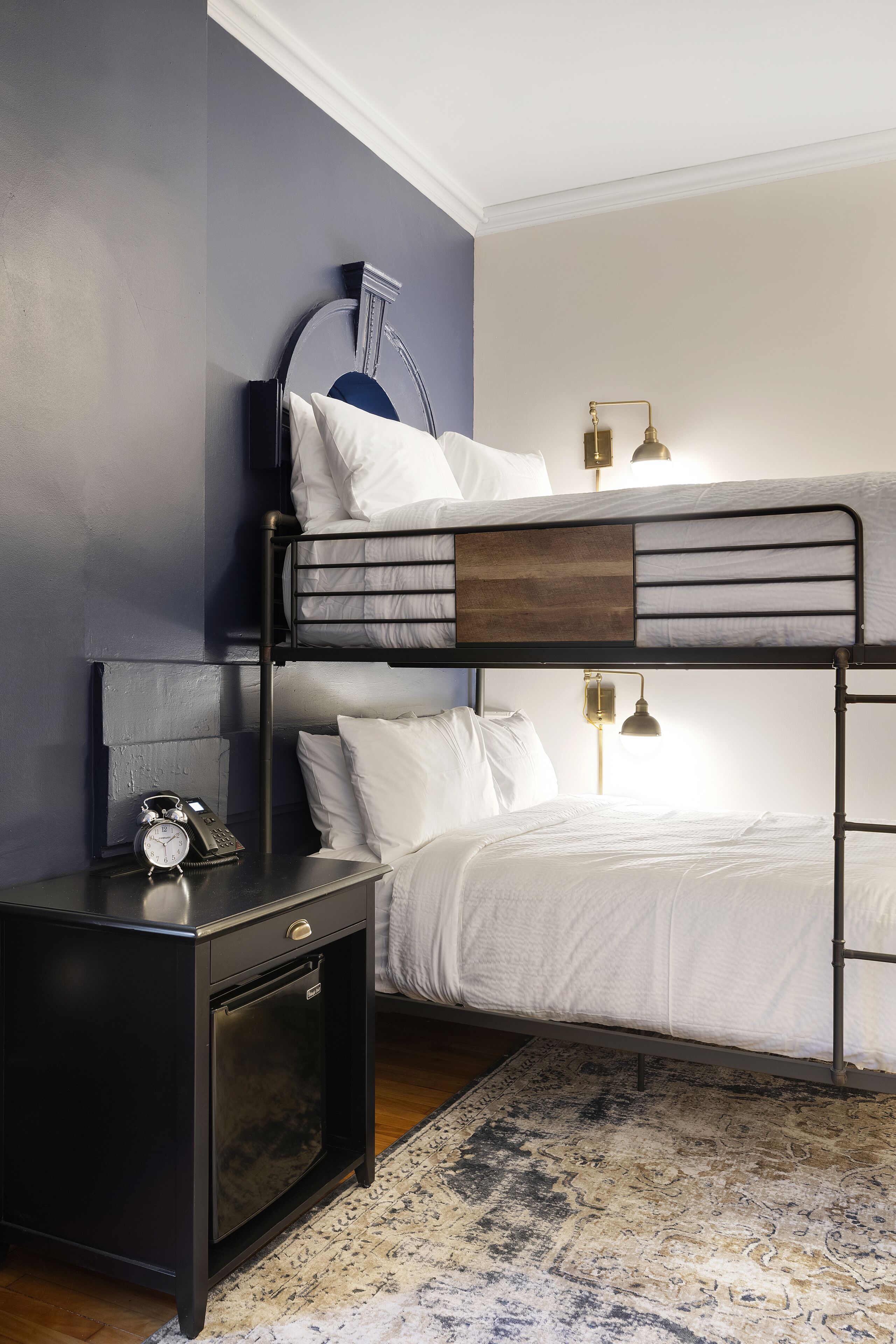 A bunk bed with white bedding, a small bedside table with a clock, and a lamp.