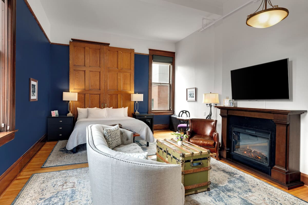 A bedroom with a large bed, a wooden wardrobe, a television, a fireplace, and a leather armchair.