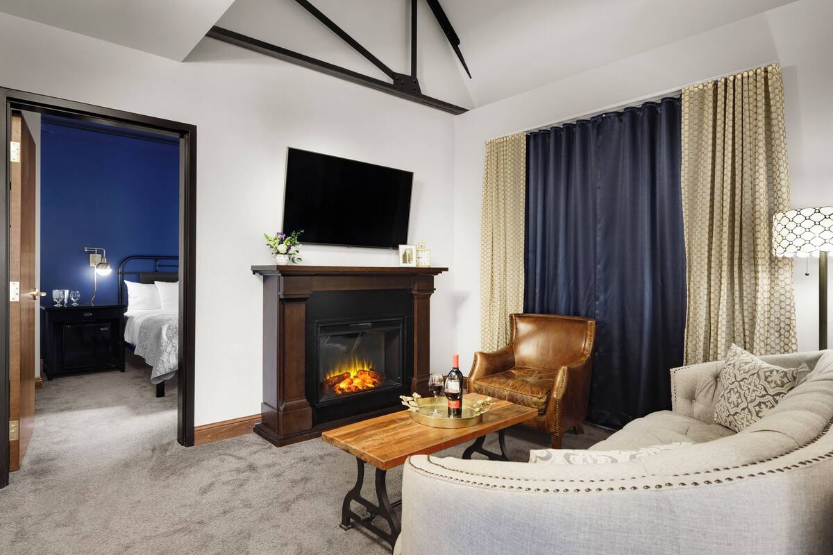 A cozy living room with a fireplace, a comfortable sofa, a leather armchair, and a flat-screen TV mounted above the fireplace.