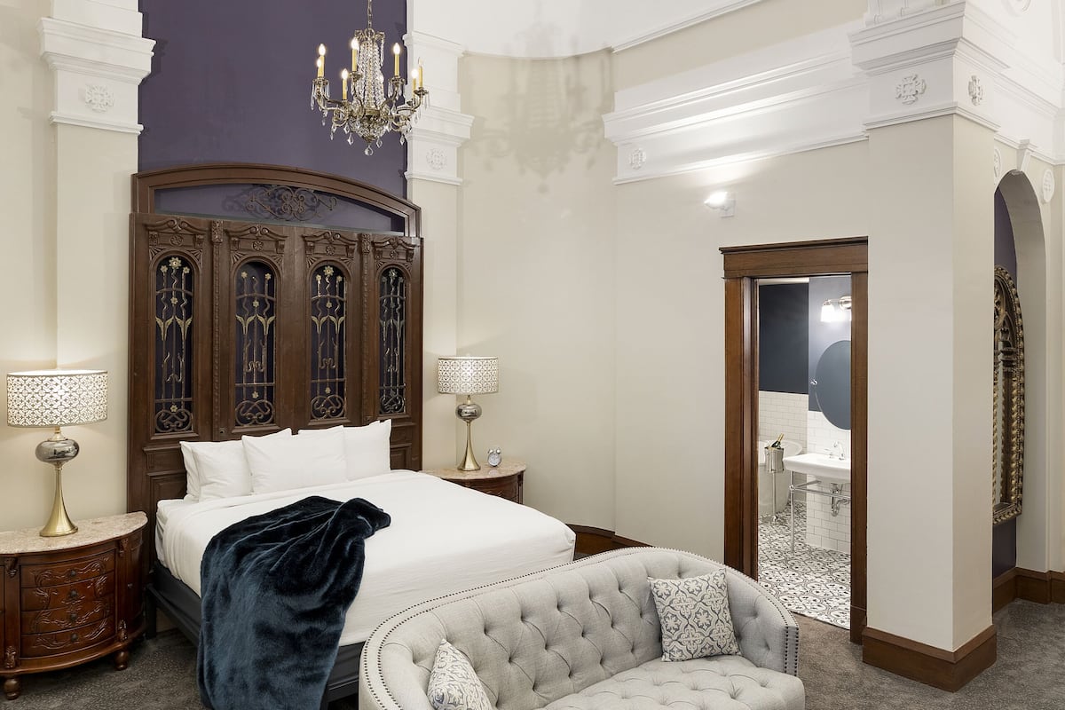 A bedroom with a large bed, a sofa, a glass coffee table, and a chandelier.