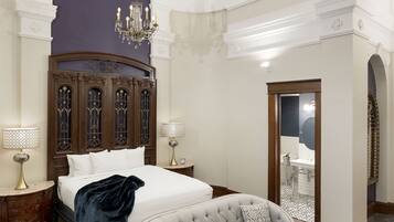 A bedroom with a large bed, a sofa, a glass coffee table, and a chandelier.