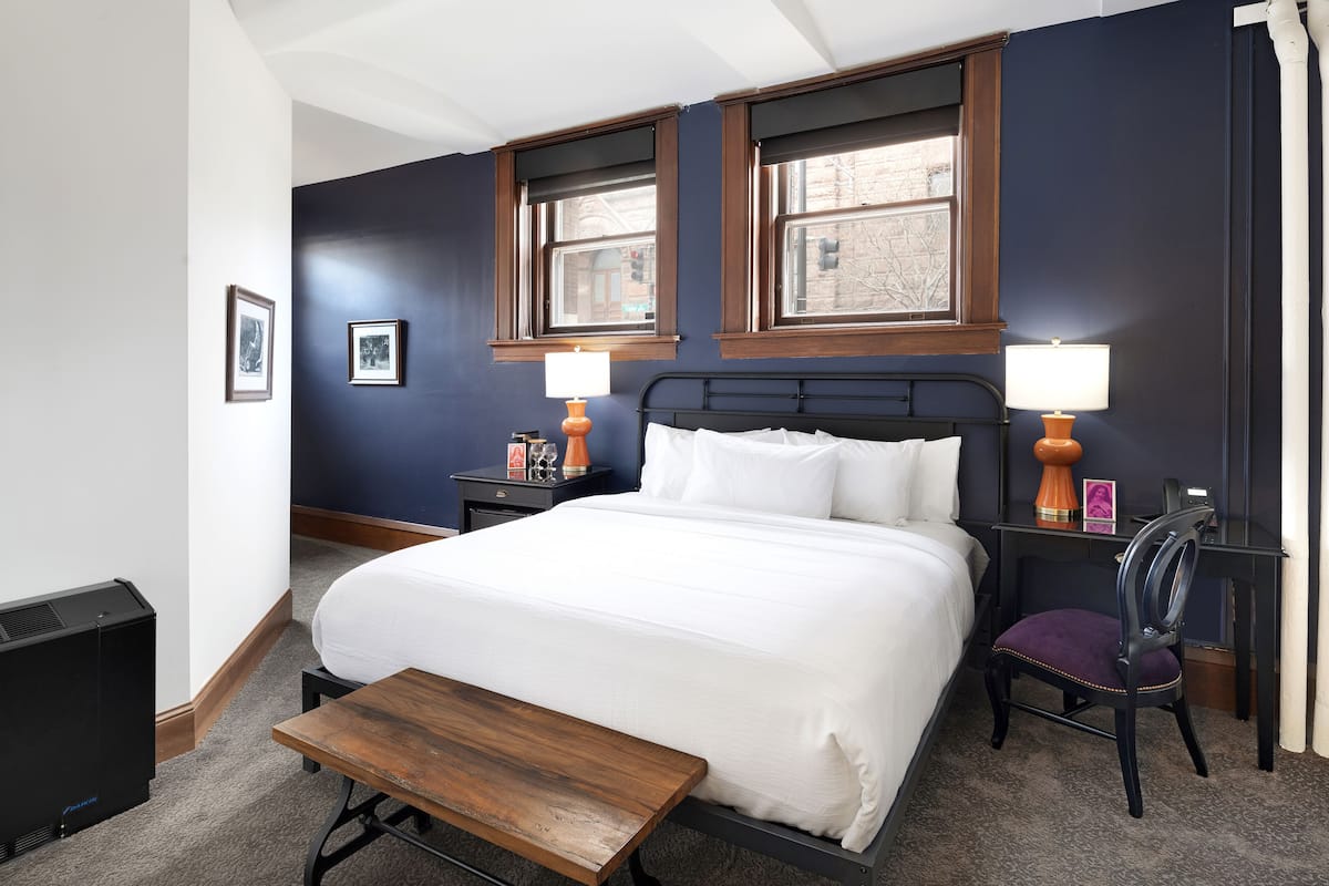 A neatly arranged hotel room with a bed, bedside tables, a chair, and a small table.
