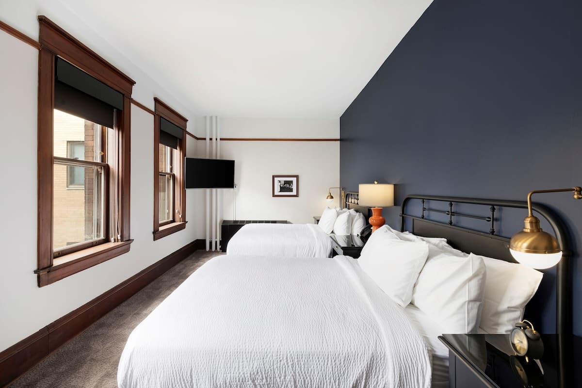 A hotel room with two beds, a flat-screen TV, bedside lamps, and a large window.