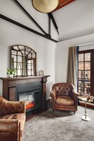 Una habitación con chimenea, un sillón de cuero, un sofá y una ventana con vistas al exterior.