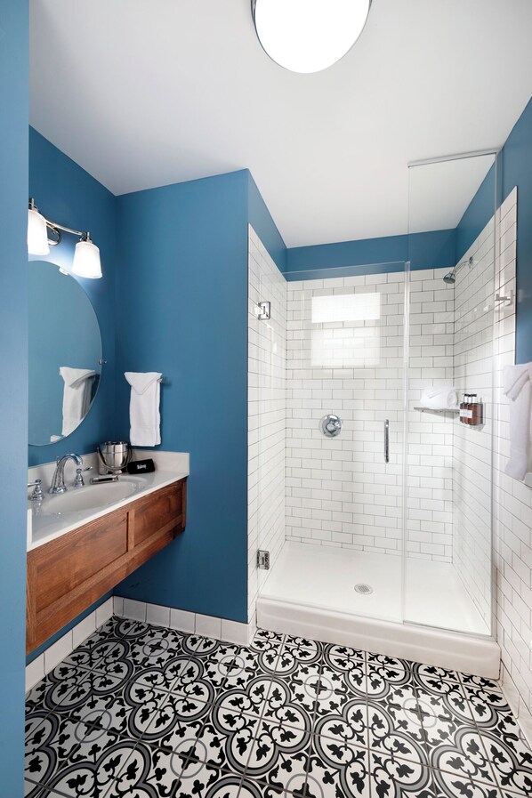 A bathroom with a blue wall, a white sink, a mirror, and a shower with white tiles.
