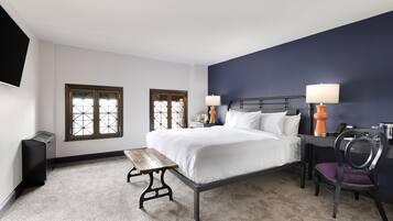A bedroom with a bed, two bedside tables, a bench, a chair, and a TV mounted on the wall.