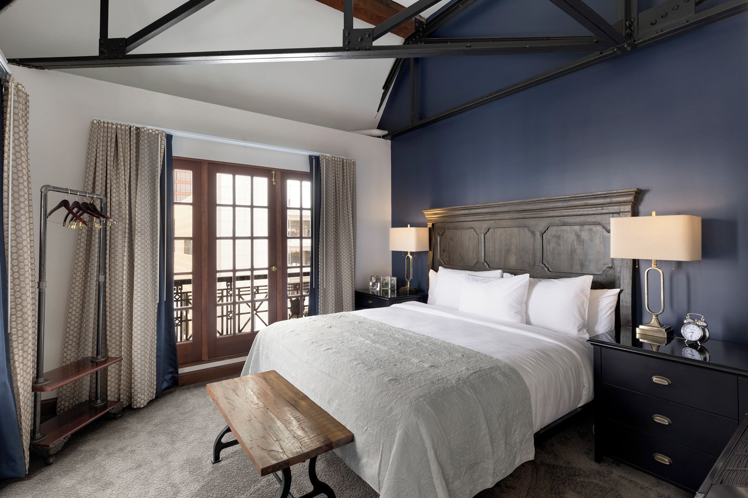 A bedroom with a large bed, bedside lamps, a wooden bench, and a view through a door.