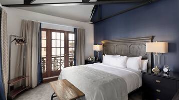 A bedroom with a large bed, bedside lamps, a wooden bench, and a view through a door.