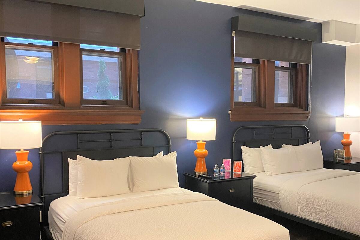 A hotel room with two beds, each with a white bedspread and pillows, flanked by nightstands with lamps.