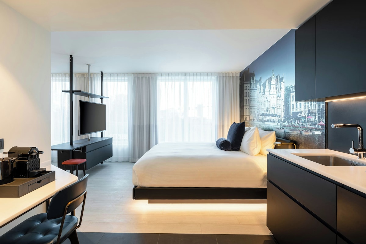 Una habitación de hotel moderna con cama, escritorio, televisor de pantalla plana y vistas a la ciudad.