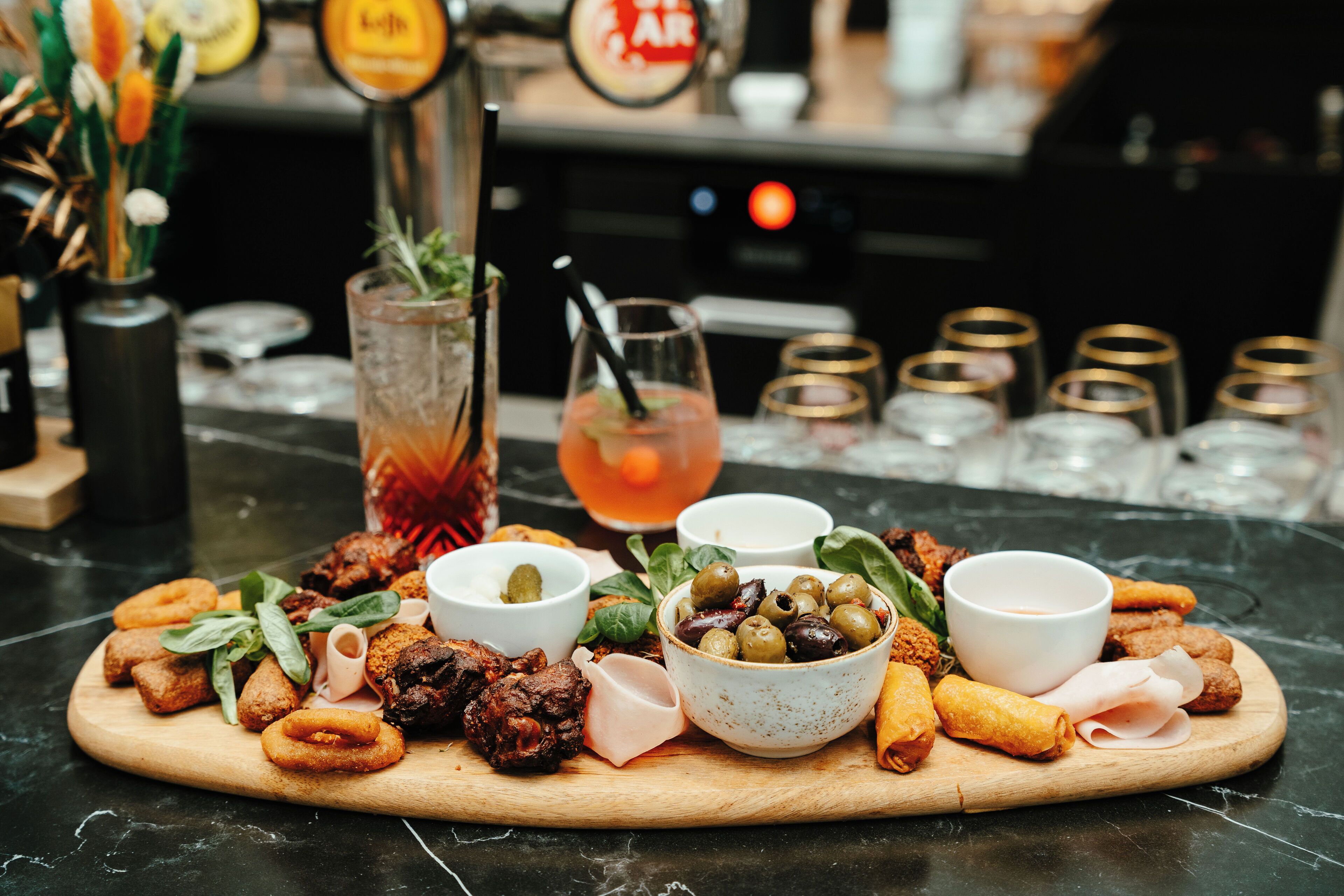 Una tabla de madera con diferentes aperitivos y bebidas sobre una encimera de mármol.