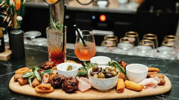 A wooden board with various appetizers and drinks on a marble countertop.