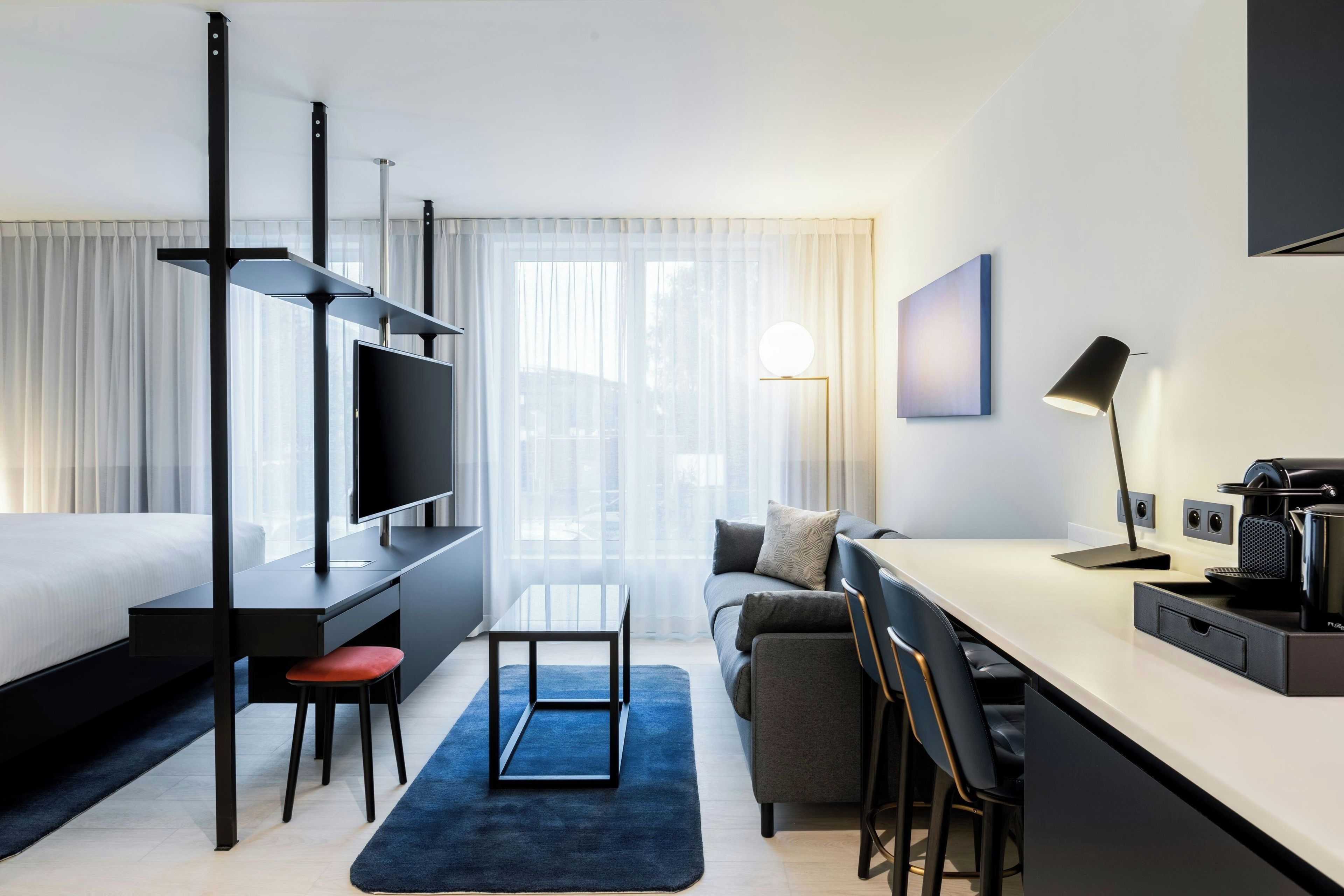 Et moderne hotelværelse med seng, skrivebord, siddeområde og et fjernsyn.