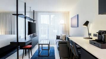 Et moderne hotelværelse med seng, skrivebord, siddeområde og et fjernsyn.