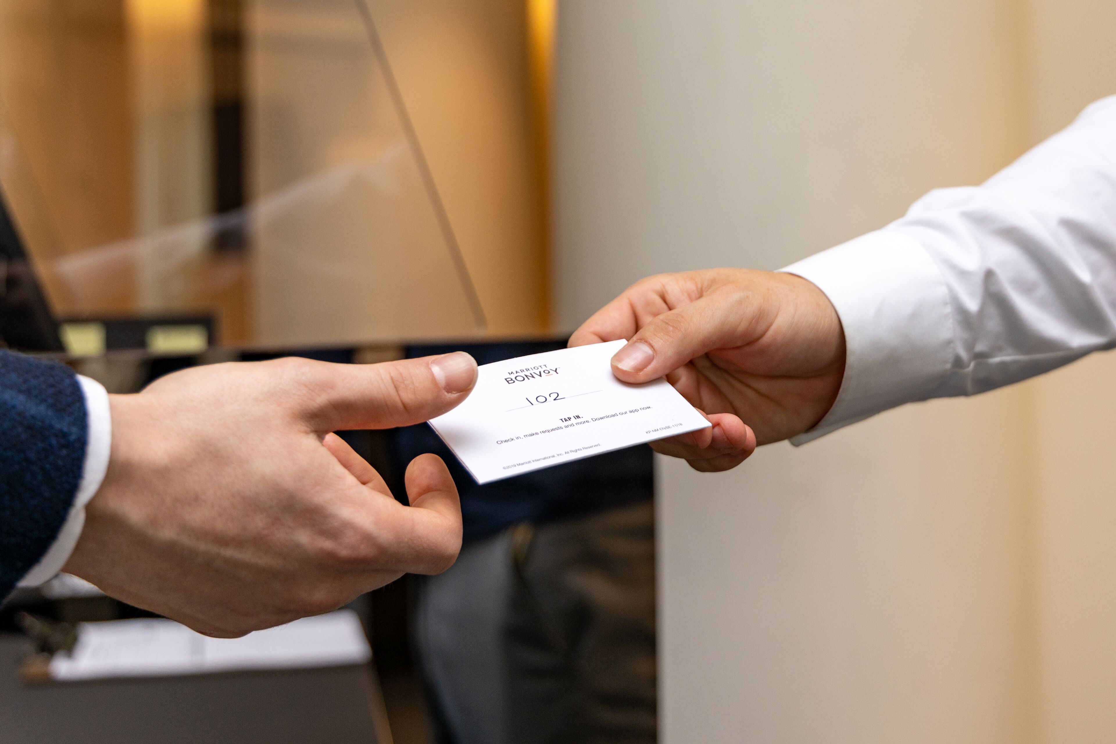 A person handing over a business card with the name "BOWY" and the number "102" to another person.