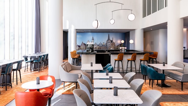 A modern restaurant with a bar area, multiple seating options including tables and chairs, and a cityscape mural on the wall.